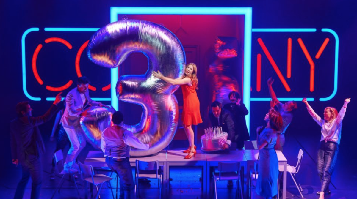 Company musical London West end The Company is set on a stage which is contemporary in design with large boxes of coloured neon lights.