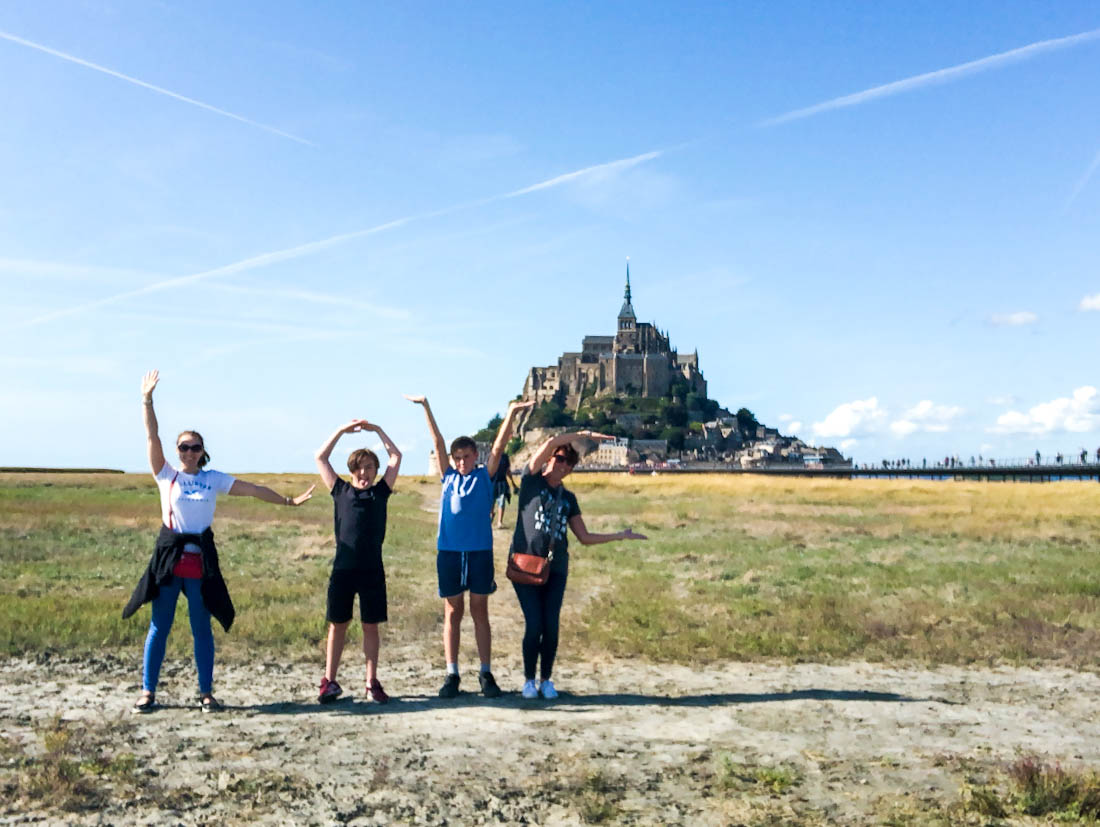 Four people doing the love sign out the front of the Mont Saint-Michel in Normandy